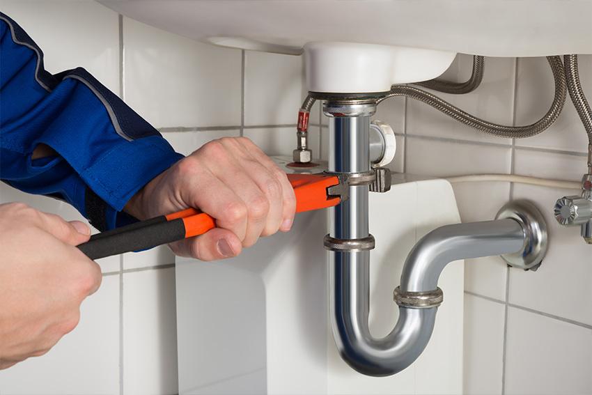 Rohrreinigung Reinickendorf – Klempner hält einen verstellbaren Schraubenschlüssel an das Siphon eines Waschbeckens